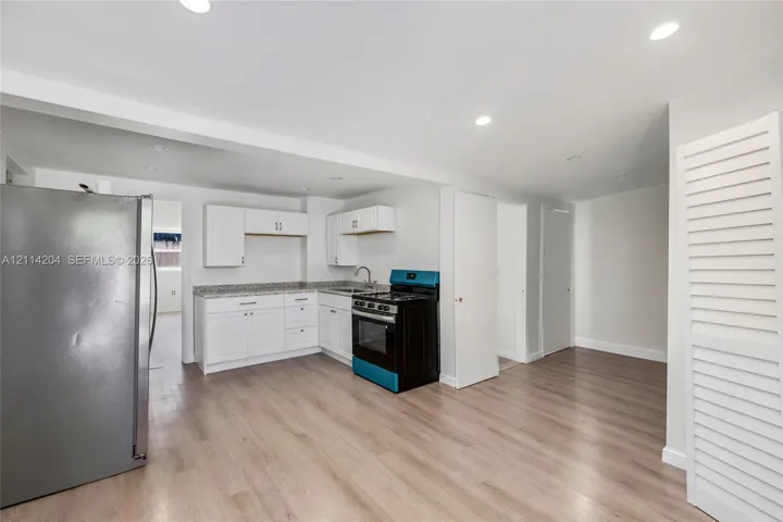Kitchen featuring white cabinetry, stone-finish countertops, stainless steel refrigerator, black range, and wood-finish flooring