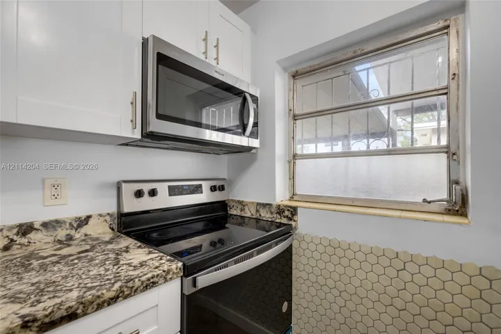 Kitchen area featuring white Shaker-style cabinetry, multi-tonal stone-composite countertops, stainless steel appliances, and a hexagonal tile backsplash