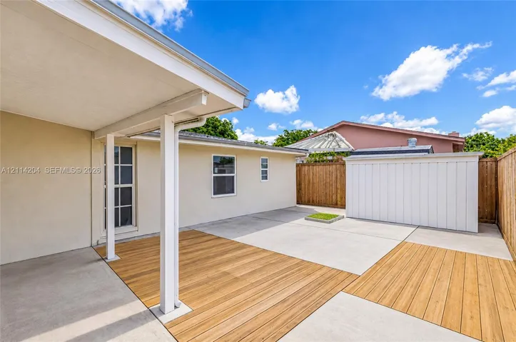 Covered concrete patio featuring wood-finish deck inlays, perimeter wood fencing, and a detached exterior storage structure
