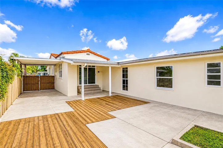 Exterior space featuring a concrete patio, integrated wood-finish decking, attached carport, and neutral stucco siding