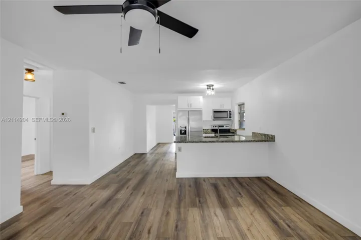 Interior featuring wood-finish flooring, white cabinetry, stone-surface countertops, built-in stainless steel appliances, and a matte black ceiling fan with integrated lighting