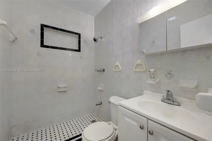 Full-bathroom featuring white wall tiling, an integrated wall niche with decorative black trim, a built-in medicine cabinet with vanity lighting, and black-and-white patterned floor tiling