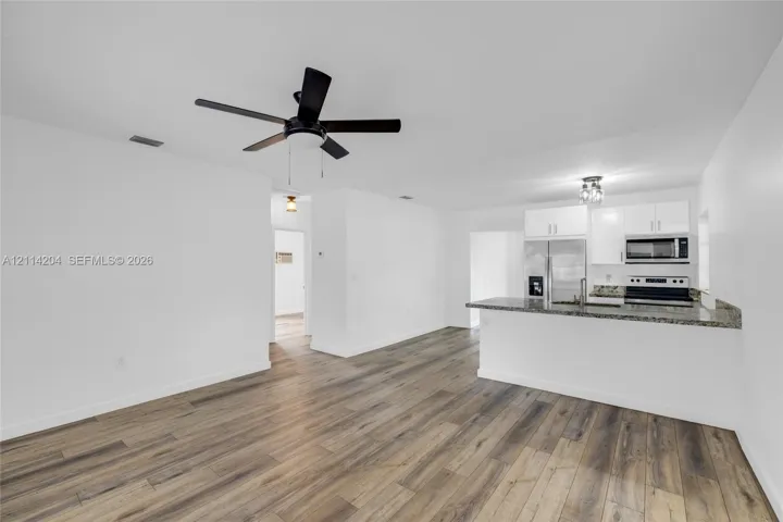 Kitchen featuring a stone-look countertop, white cabinetry, integrated microwave, and wood-finish flooring, complemented by a ceiling fan