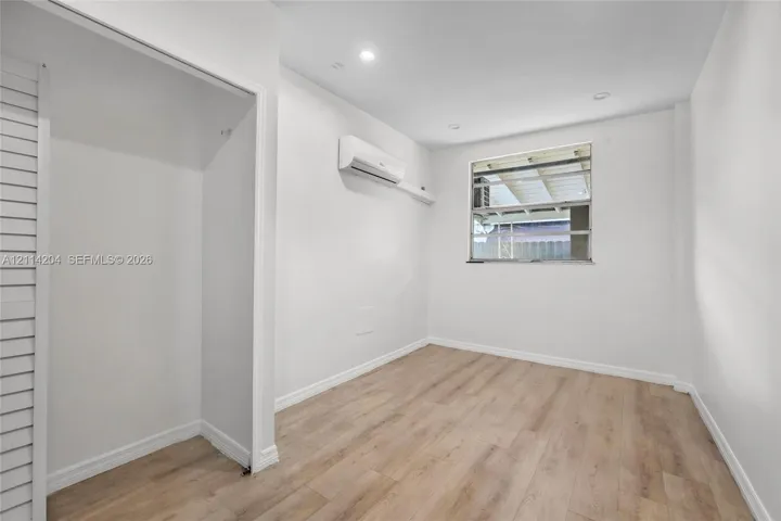 Neutral interior featuring wood-finish flooring, recessed lighting, a wall-mounted climate control unit, and a built-in closet with louvered doors