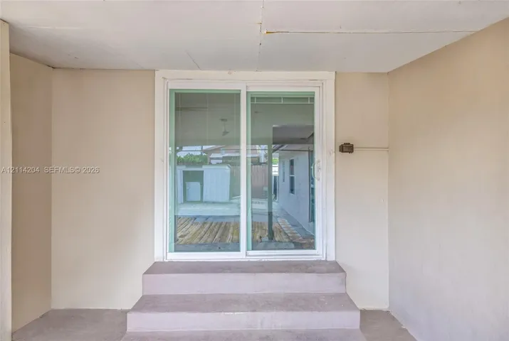 Covered concrete entryway featuring dual-panel sliding glass door with white framing and integrated concrete steps