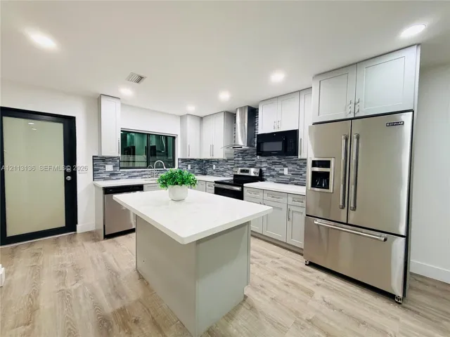 Kitchen featuring light gray shaker-style cabinetry, quartz countertops, a central island, stainless steel appliances, and a glass-tiled backsplash