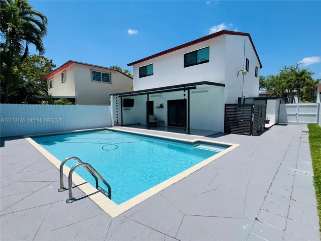 In-ground swimming pool with metal ladder, expansive concrete patio, covered outdoor living area, and white vinyl privacy fencing