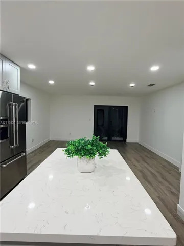 Kitchen island with a light-toned, veined countertop, stainless steel refrigerator, recessed lighting, and wood-finish flooring