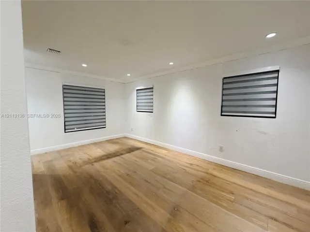 Interior space featuring wood-finish flooring, neutral wall tones, recessed lighting, and dual-layered window shades