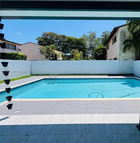 In-ground swimming pool featuring metal access ladders and a concrete pool deck enclosed by white vinyl fencing
