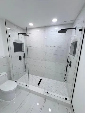 Walk-in shower featuring dual shower heads with matte black fixtures, frameless glass enclosures, built-in recessed shelving, and stone-finish wall tile
