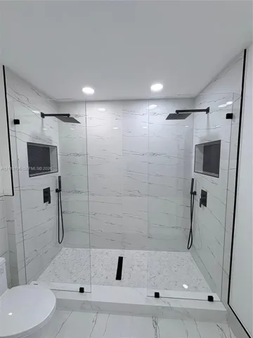 Walk-in shower featuring large-format stone-patterned tile walls, dual rainfall showerheads, handheld sprayers, built-in recessed niches, and matte black hardware