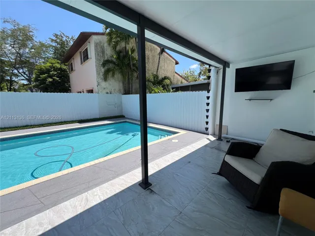 Covered patio featuring large-format tile flooring, swimming pool with tiled coping, and white vinyl privacy fencing