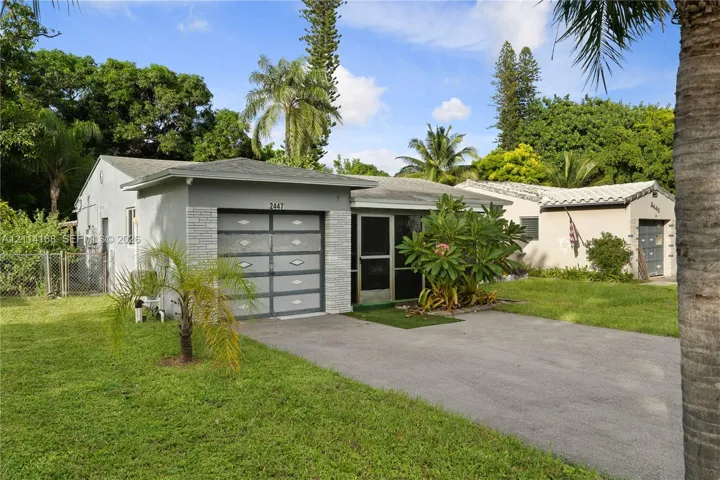 Single-story residence, textured exterior siding, and a paved driveway, surrounded by a lawn with mature trees and vegetation