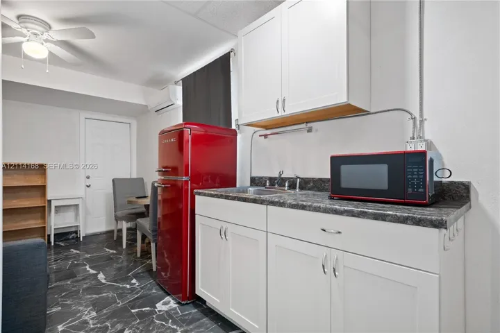 Kitchenette area featuring white shaker-style cabinetry, dark stone-finish countertops, stainless steel sink, wall-mounted ductless climate control unit