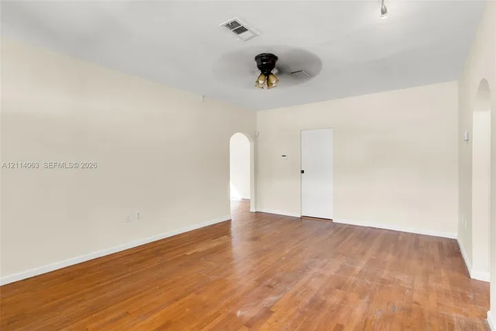 Neutral-toned interior space featuring wood-finish flooring, an arched entryway, and a ceiling fan with multi-light fixture