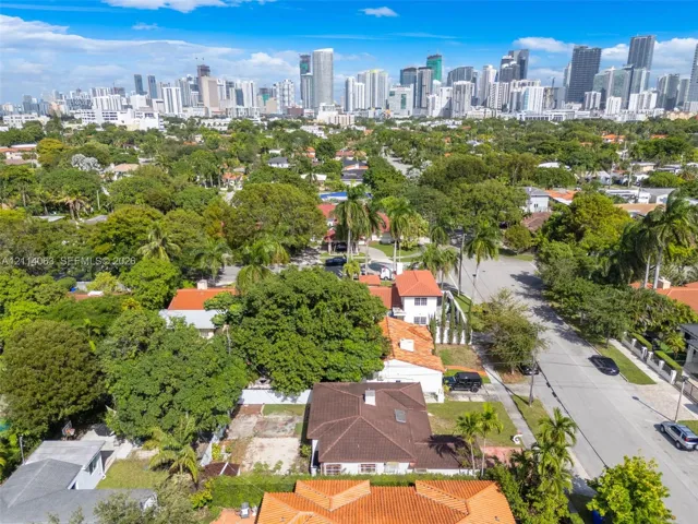 Aerial perspective showcasing a residential lot with mature trees, established landscaping, and an expansive urban skyline backdrop