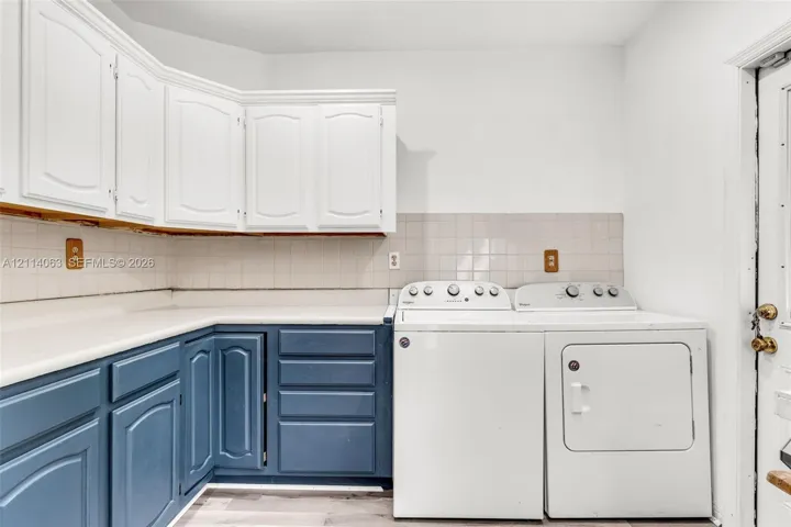 Laundry room featuring two-tone cabinetry, solid surface countertops, square tile backsplash, and wood-finish flooring
