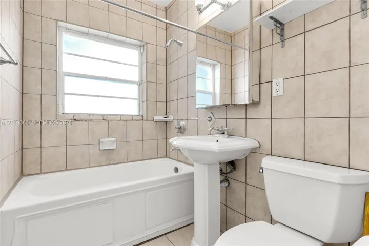 Bathroom featuring ceramic wall tiling, white porcelain pedestal sink, built-in bathtub, and integrated medicine cabinet with mirror