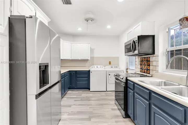Kitchen featuring stainless steel appliances, blue and white cabinetry, wood-finish flooring, double-basin sink, and integrated laundry area