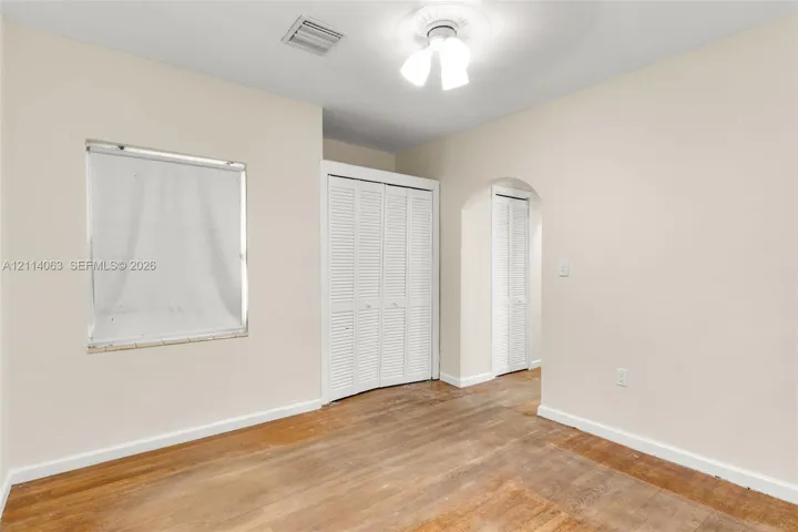 Interior room featuring wood-finish flooring, white louvered closet doors, a structural arched doorway, and a ceiling-mounted light fixture with a decorative medallion