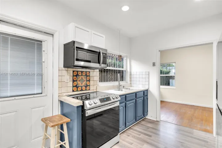 Kitchen featuring stainless steel appliances, blue lower cabinetry, white upper cabinetry, square-tile backsplash, and wood-finish flooring