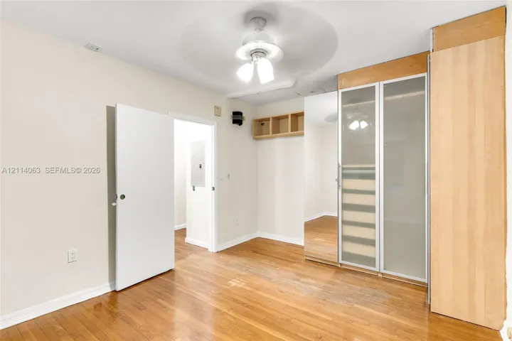 Wood-finish flooring, built-in floor-to-ceiling cabinetry with frosted glass panels, mirrored closet doors, open wall-mounted shelving, and a central ceiling fan with multi-light fixture