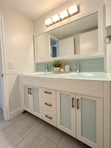 Double vanity featuring frosted glass cabinet doors, integrated glass countertop with dual sinks and light blue subway tile backsplash