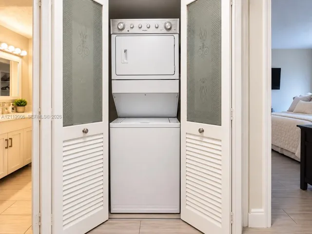 Stacked white laundry center enclosed behind louvered bi-fold doors with frosted decorative glass panels