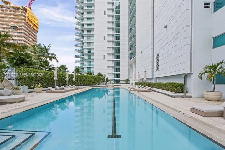 Lap pool featuring a stone-paver deck, built-in tile lane marker, manicured hedges, and high-rise building exterior