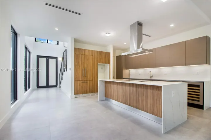 Modern kitchen featuring a waterfall-edge island, panel-ready cabinetry, stainless steel ventilation hood, under-cabinet lighting, and large-format tile flooring