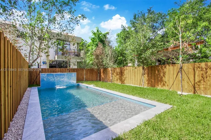 Private backyard featuring a rectangular swimming pool with a mosaic tile water feature, stone-finish coping, mature landscaping, and a wood privacy fence