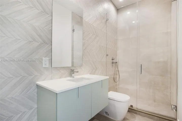 Bathroom featuring a floating vanity with a stone-top integrated sink, wall-to-wall chevron patterned tile wall, glass-enclosed shower, and modern dual-flush toilet
