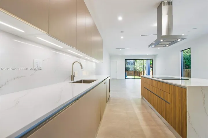Modern kitchen featuring slab-front cabinetry, quartz countertops with full-height backsplash, undermount sink with arched faucet, stainless steel chimney-style range hood, and integrated induction cooktop