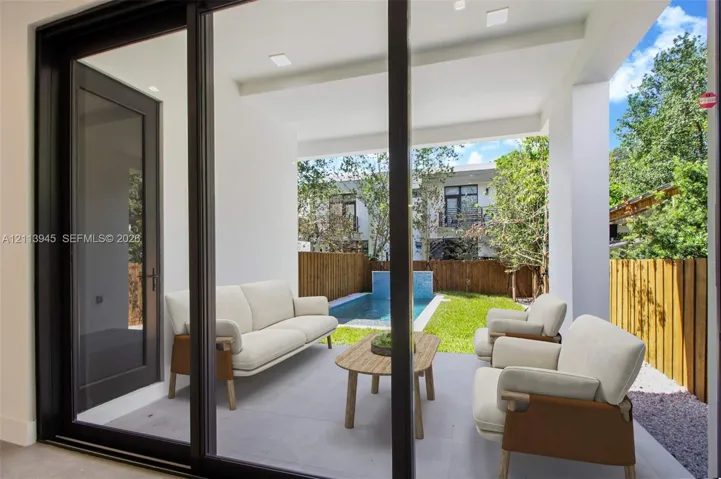 Covered patio with large-format tile flooring, oversized black-framed glass sliding doors, private swimming pool, and wood privacy fencing