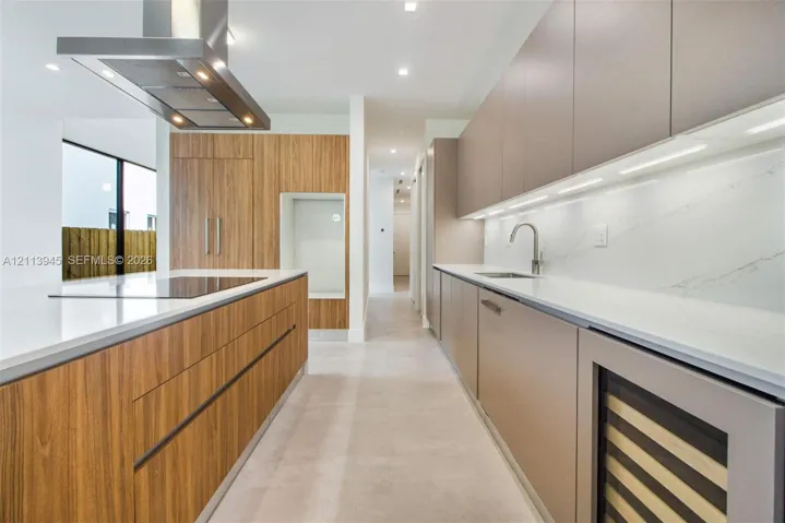 Modern kitchen featuring wood-finish cabinetry, waterfall-edge quartz countertops, stainless steel range hood, under-cabinet lighting, and built-in wine refrigeration