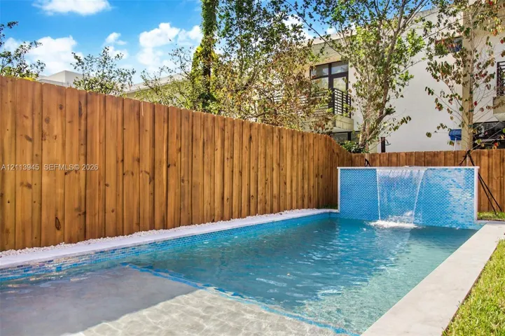 Swimming pool featuring a blue tile water feature, white stone border, and vertical wood privacy fencing