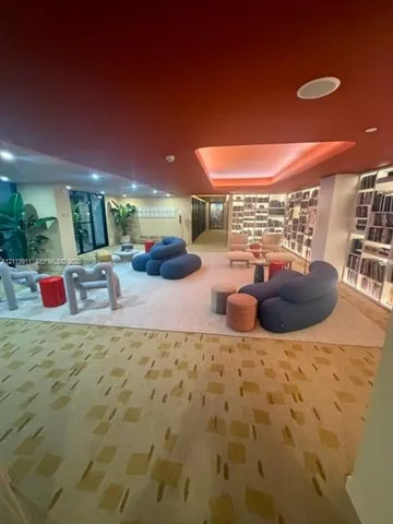 Expansive room featuring floor-to-ceiling wall-to-wall library shelving, recessed tray ceiling lighting, and patterned carpeting