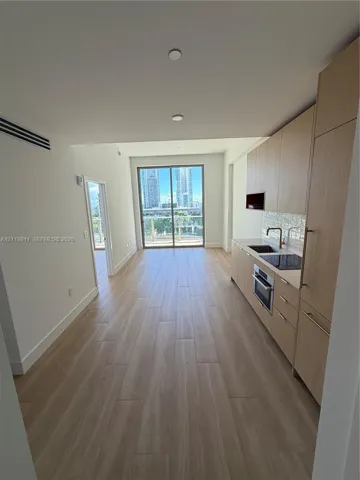 Kitchen featuring light-tone wood cabinetry, built-in cooktop and oven, integrated refrigerator, and wood-finish flooring with floor-to-ceiling glass sliding doors