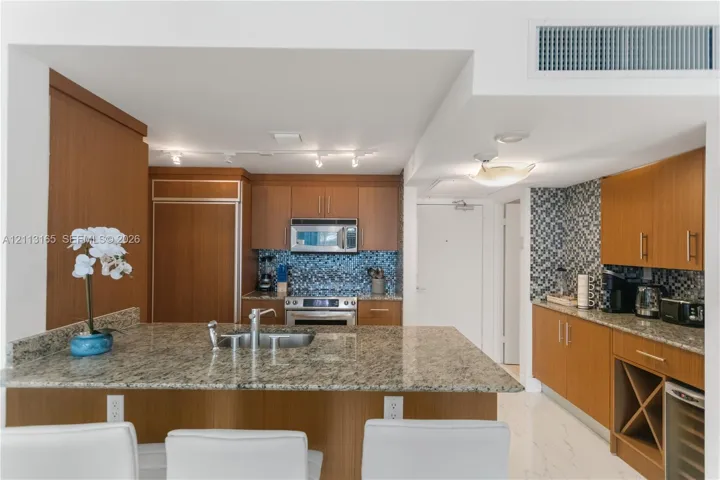 Kitchen featuring wood-finish cabinetry, stone countertops, mosaic tile backsplash, built-in stainless steel appliances, and a dedicated wine storage rack