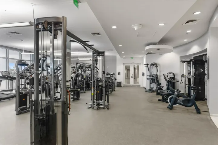 Fitness facility featuring rubberized flooring, recessed ceiling lighting, full-length mirrors, and glass double doors