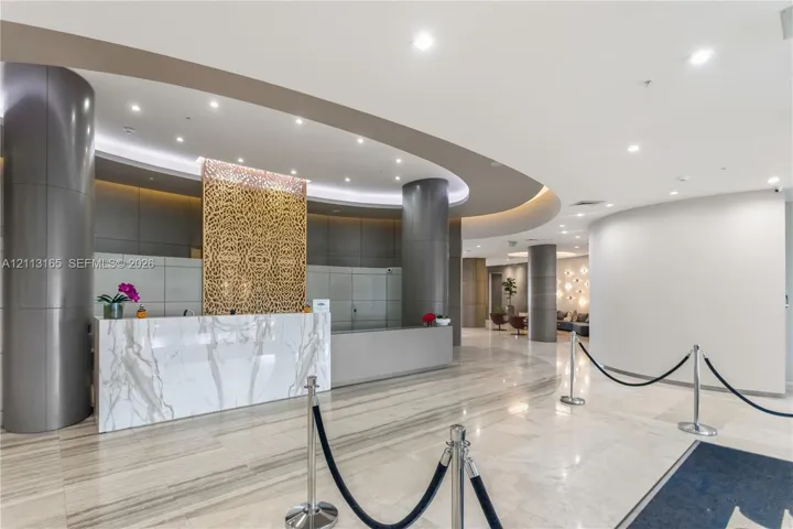 Grand lobby featuring stone-surfaced reception desk, recessed ceiling lighting, decorative metal lattice wall paneling, and polished stone flooring