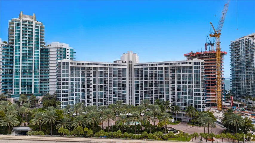High-rise residential building featuring floor-to-ceiling glass paneling, extensive private balcony configurations, and landscaped grounds with mature palm trees