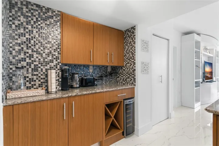 Custom cabinetry featuring integrated wine storage, stone countertops, a mosaic tile backsplash, and built-in shelving