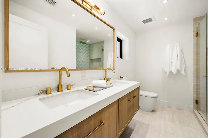 In suite Bathroom Double vanity featuring wood-finish cabinetry, white countertop with dual undermount sinks, gold-tone fixtures, and a large wood-framed mirror