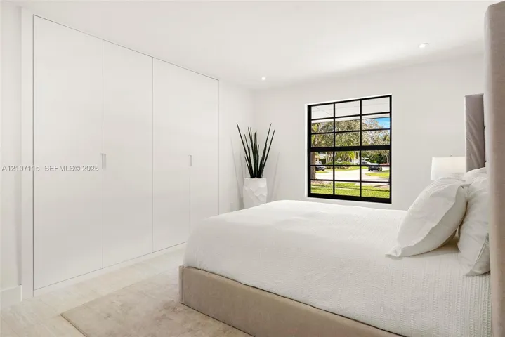 Bedroom 3 Full-wall built-in cabinetry with flush-panel doors, grid-pattern window with matte black frame, recessed ceiling lighting, and neutral stone-finish flooring