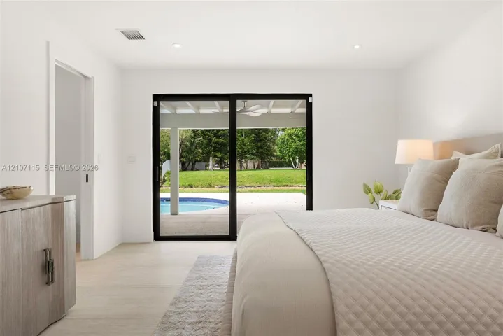 Light-filled interior featuring sliding glass doors with black frames, neutral stone-finish flooring, and recessed lighting