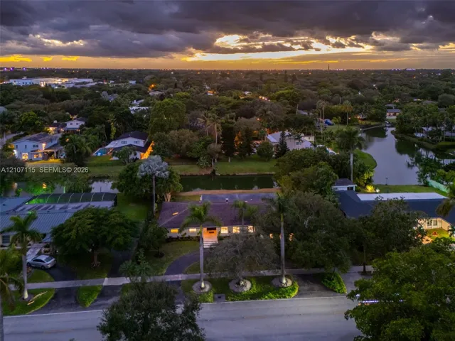 Aerial perspective featuring a waterfront property with established landscaping, mature palm trees, and a paved driveway