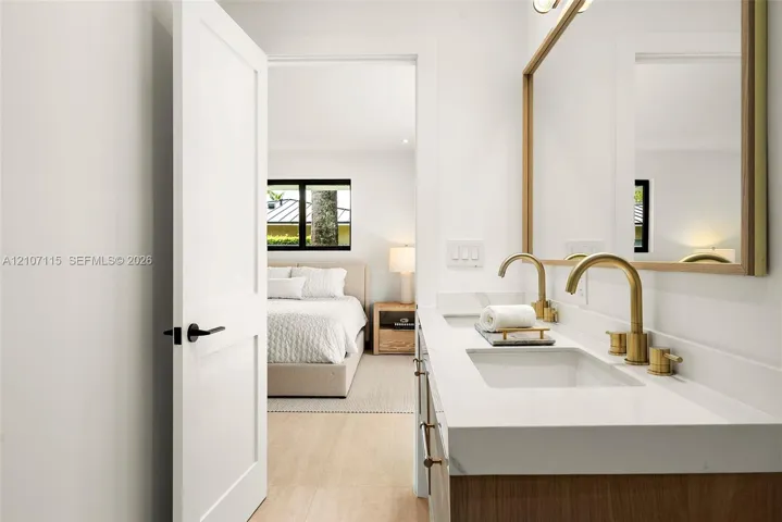 Dual-sink vanity with quartz countertop, brass-toned fixtures, wood-finish cabinetry, and a large framed mirror