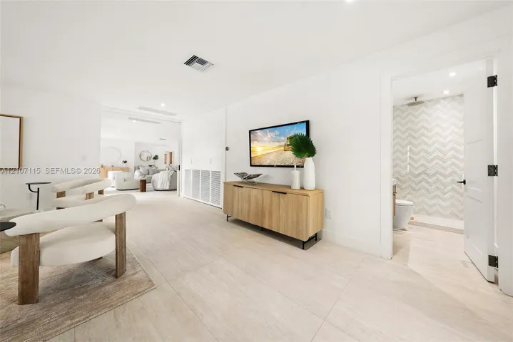 Family room/ 5 bedroom in suite Large-format tile flooring throughout featuring light neutral tones, recessed lighting, and a bathroom showcasing chevron-patterned wall tile with a rain-style shower head
